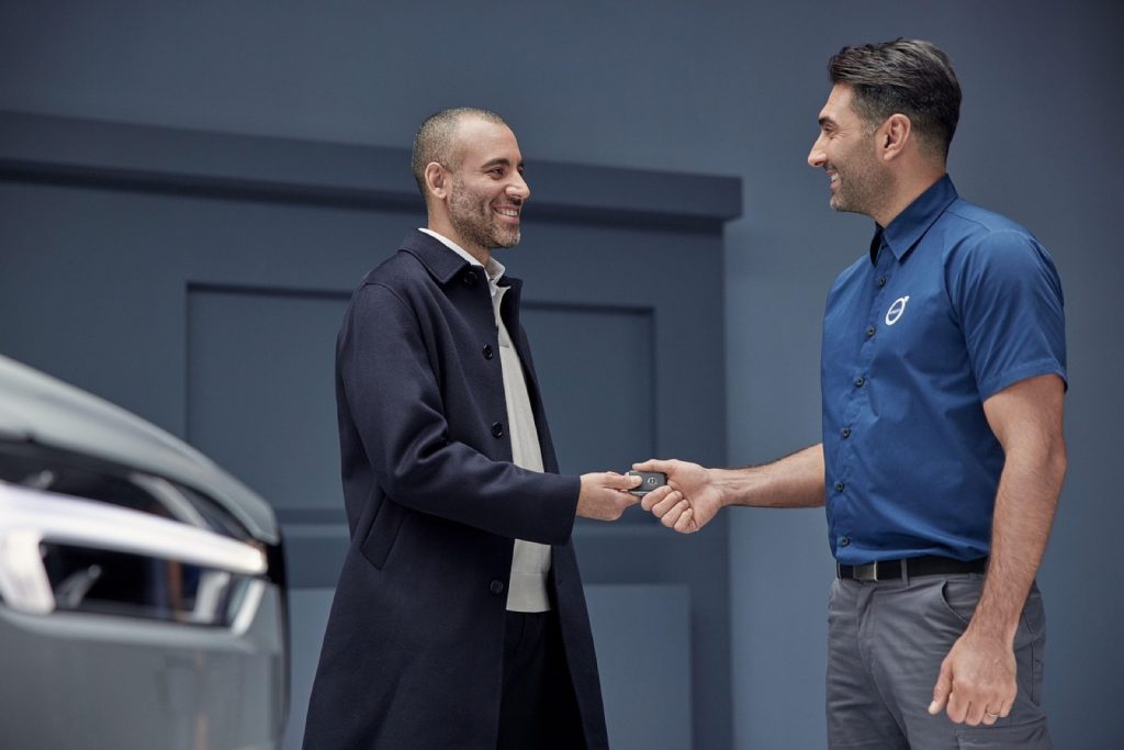 Two people shaking hands beside a car at a dealership