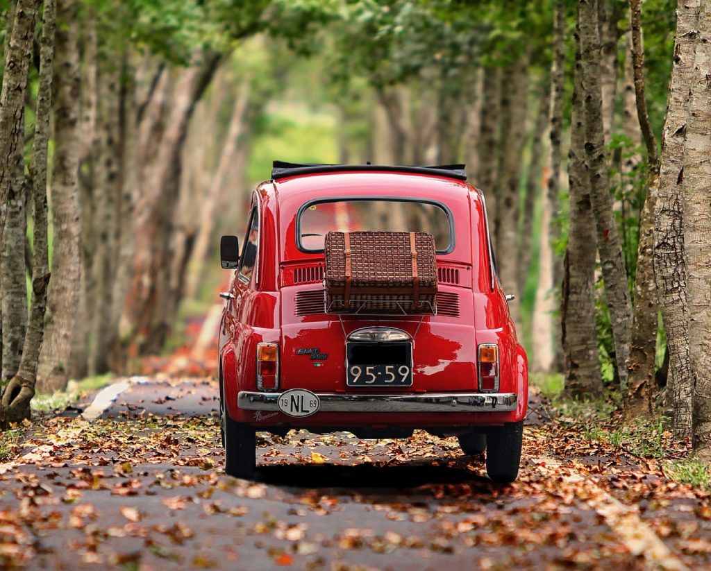 A small red car parked on a tree-lined road
