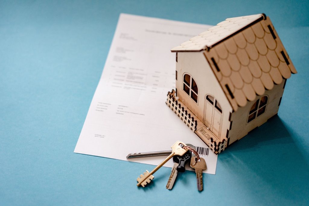 A small wooden model house and a set of keys resting on a printed document