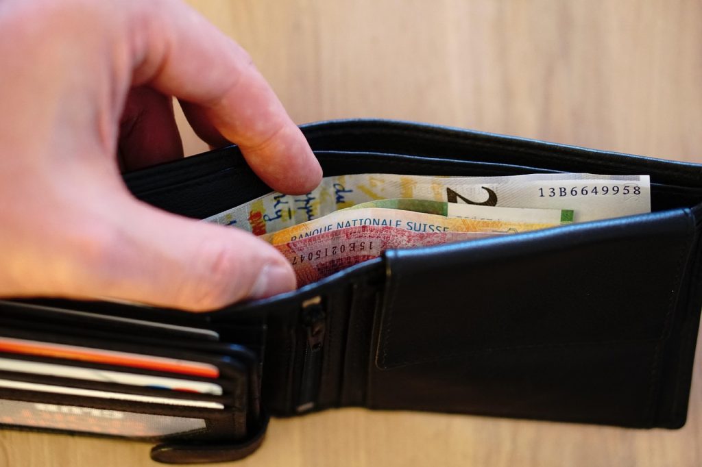 A hand taking a banknote from a leather wallet